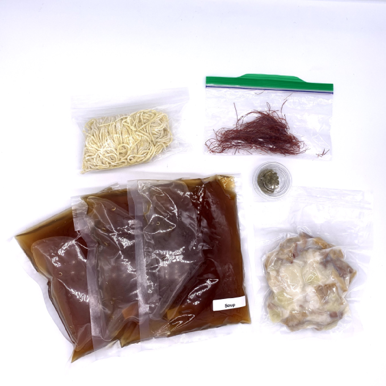 3 shoyu soup packages with vacuum packed offal, noodles in zip bag, shredded chilli in zip bag and yuzu pepper in small container.